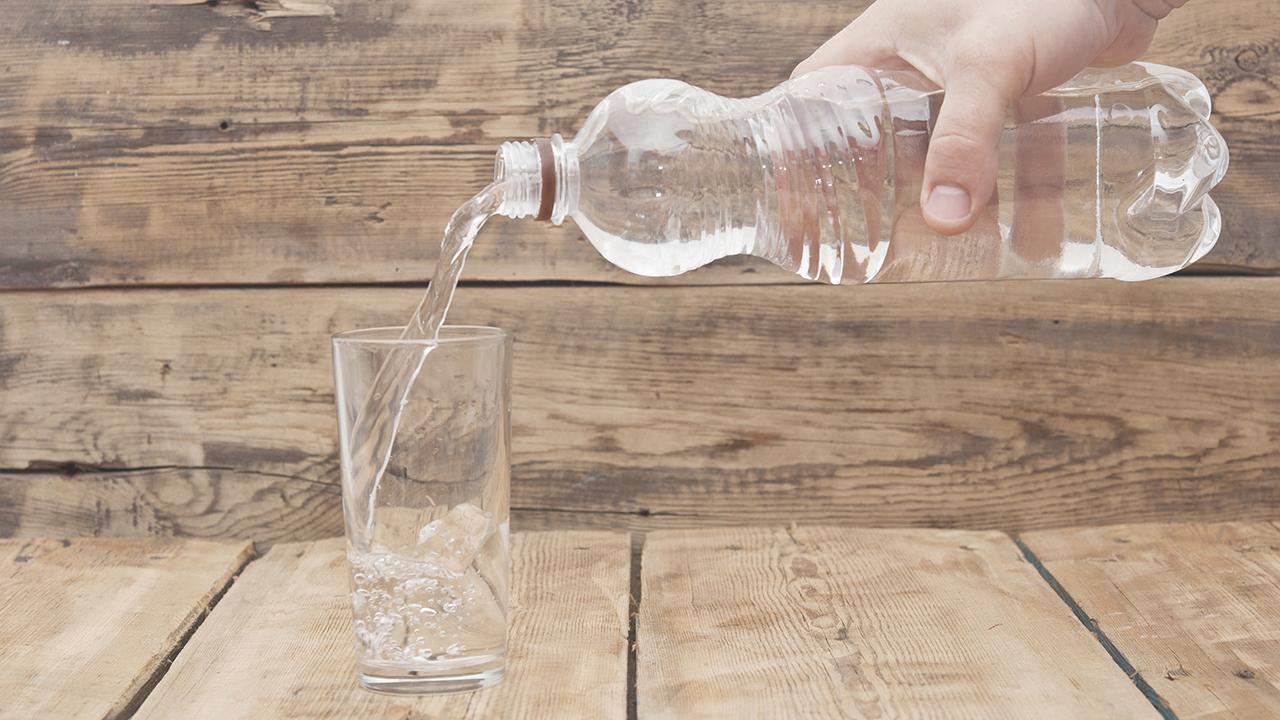 Hånd holder vandflaske og hælder op i et glas.